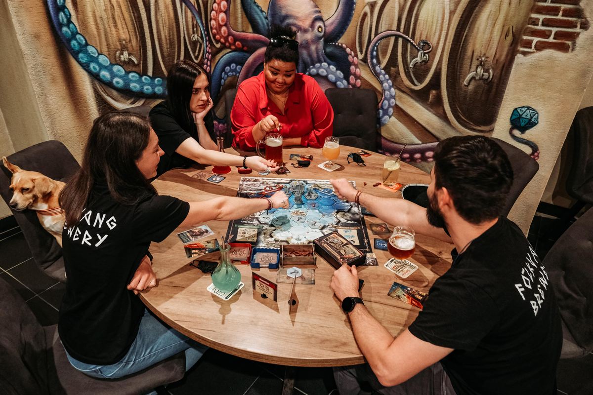 Four players at a board game under the U Krakena octopus mural